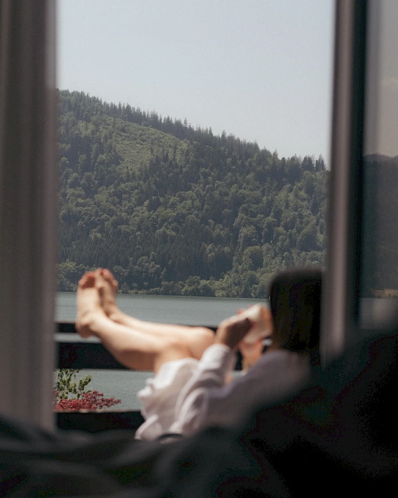 Woman in a bathrobe enjoying coffee on the balcony, taking in the view of Schliersee and the mountains.