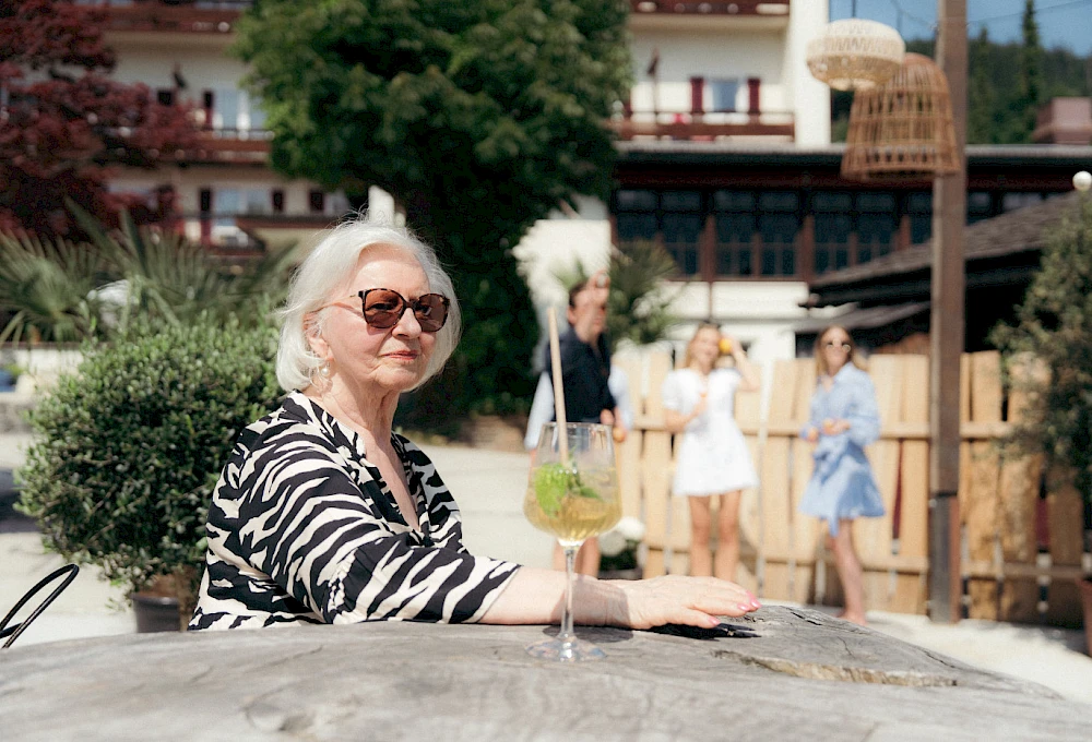 Woman enjoying a summer drink in front of the lake hotel, a group of young people in the background.