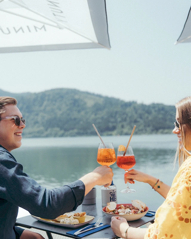 Couple toast and enjoy delicious food with a view of Lake Schliersee.