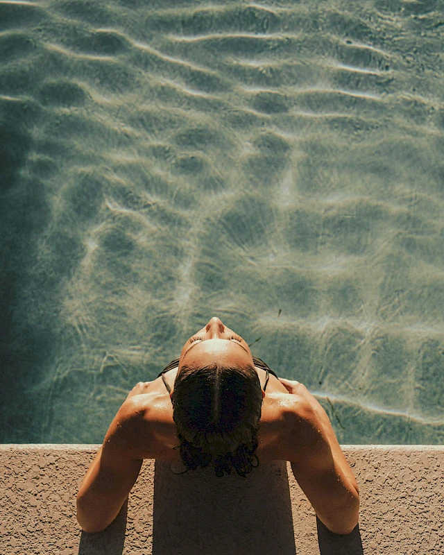 Woman in a pool enjoying the evening sun on her face.
